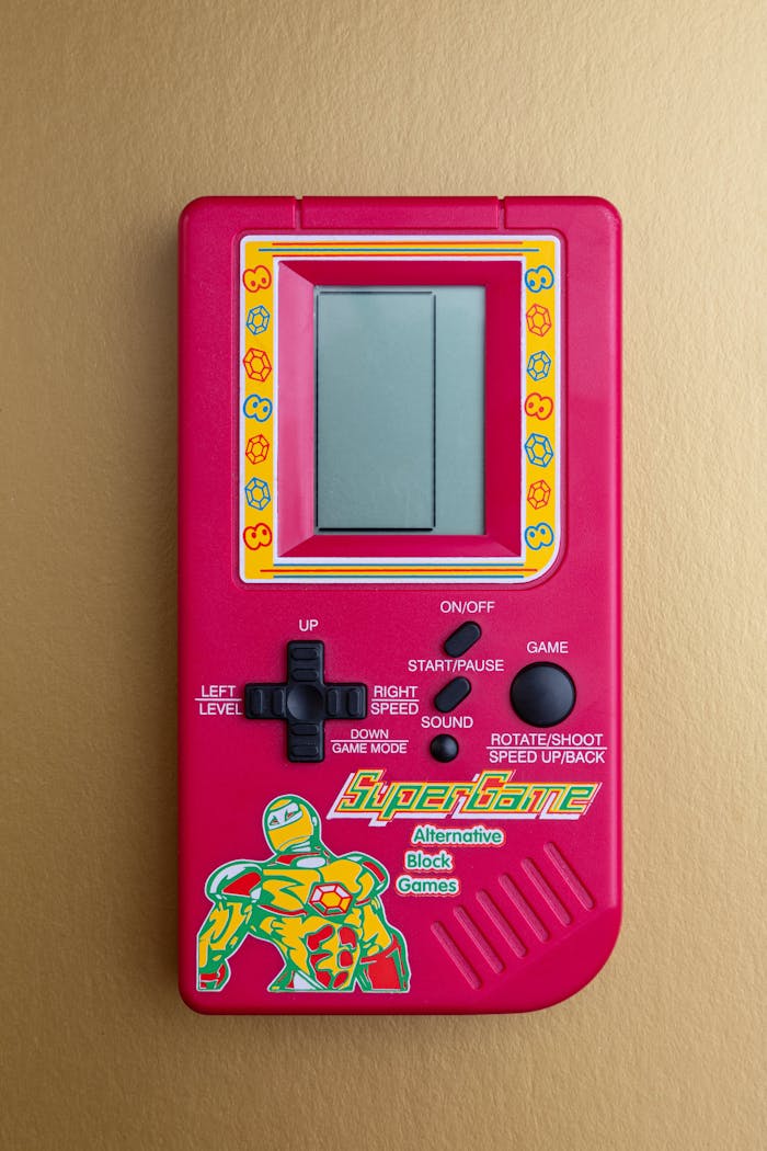 Red vintage handheld game console with colorful buttons on a gold surface, evoking nostalgia.