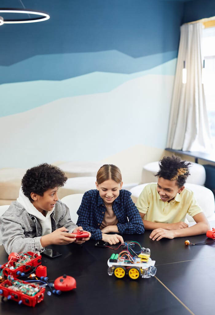 Three children building and playing with robotics at a table indoors.
