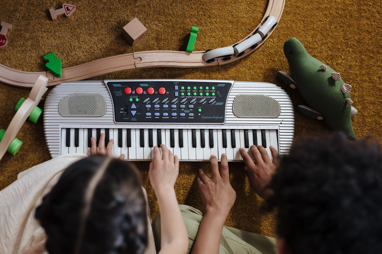 Top view of children playing keyboard with toy train and plush dinosaur on the floor.